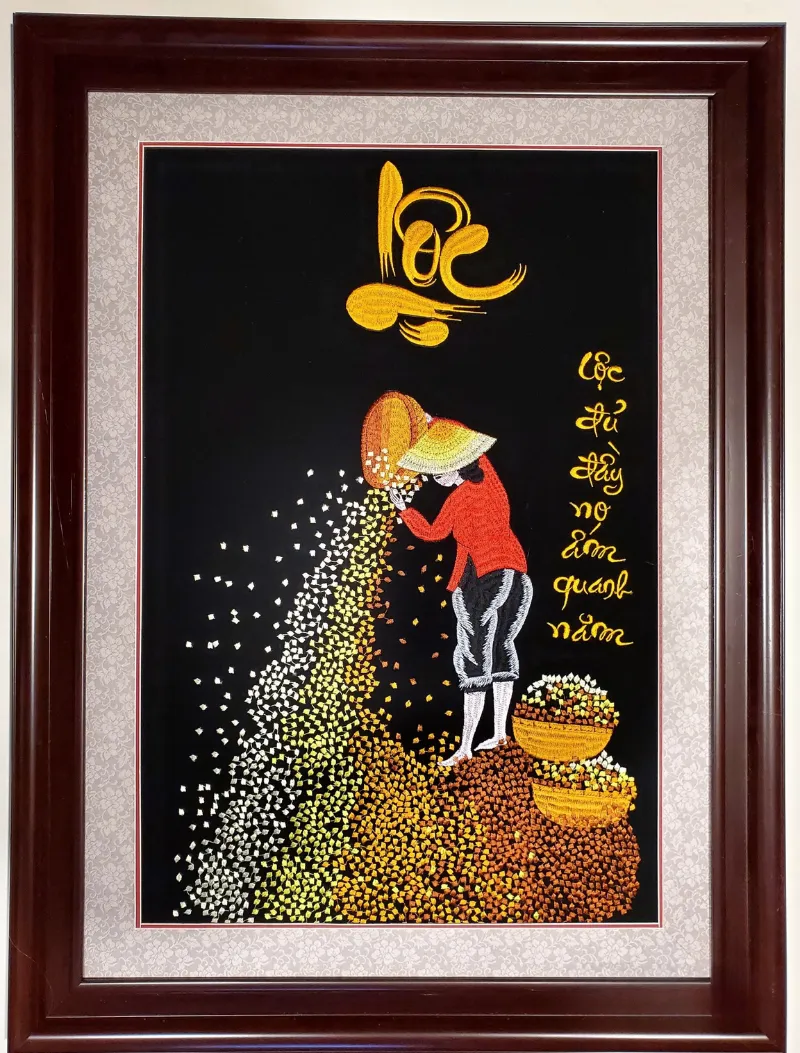 Tranh thêu thư pháp "Lộc" với hình ảnh người phụ nữ đang đổ những hạt lúa vàng óng, thể hiện sự sung túc, ấm no